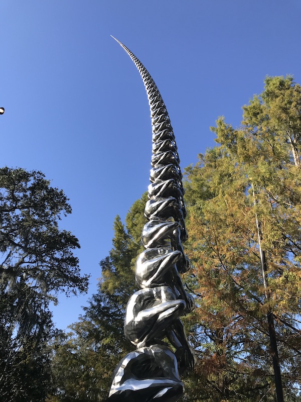 A steel tower sculpture of people on top of one another at the Bestoff Sculpture Garden
