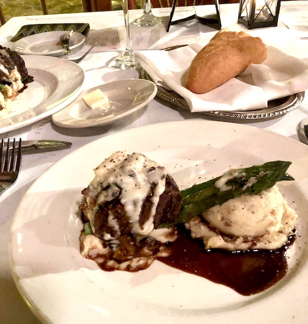 A filet mignon topped with creamy sauce along side are mashed potatoes and asparagus on a white plate at Café Vermillionville Lafayette Louisiana