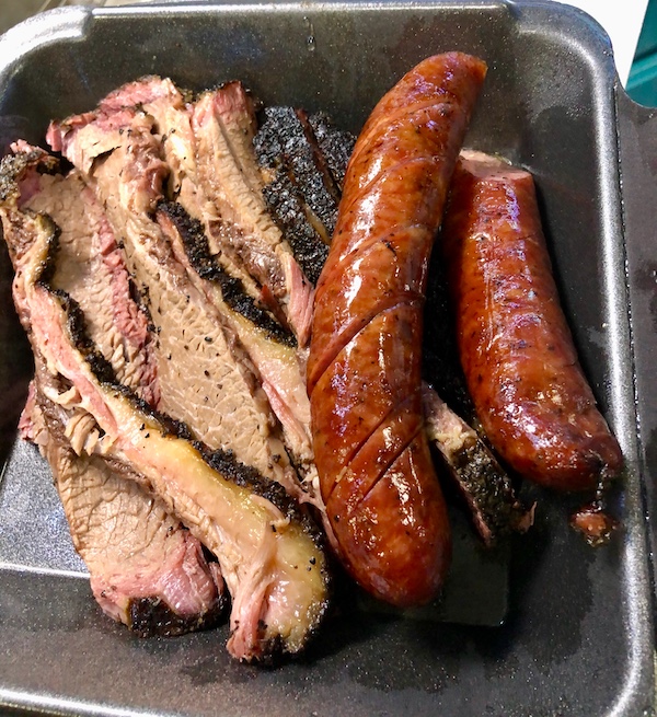 A black take out container filled with sliced brisket and sausages near the Holocaust Museum Houston