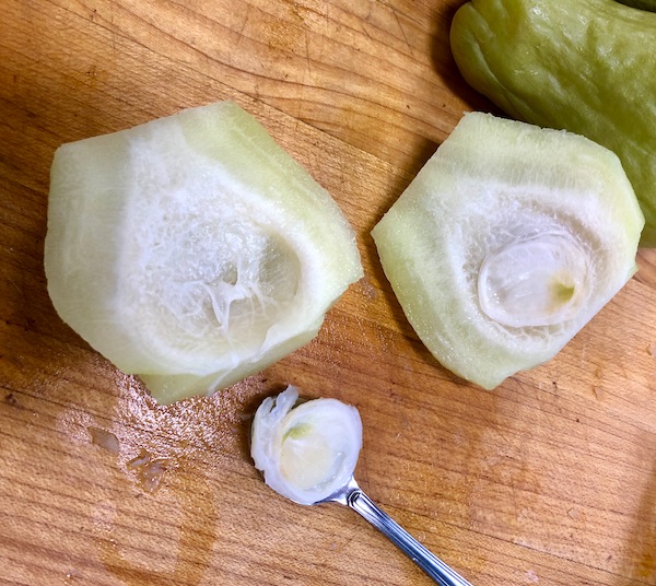 Seasonal Ingredient Mirliton cut in half with one seed removed and sitting in a small spoon.