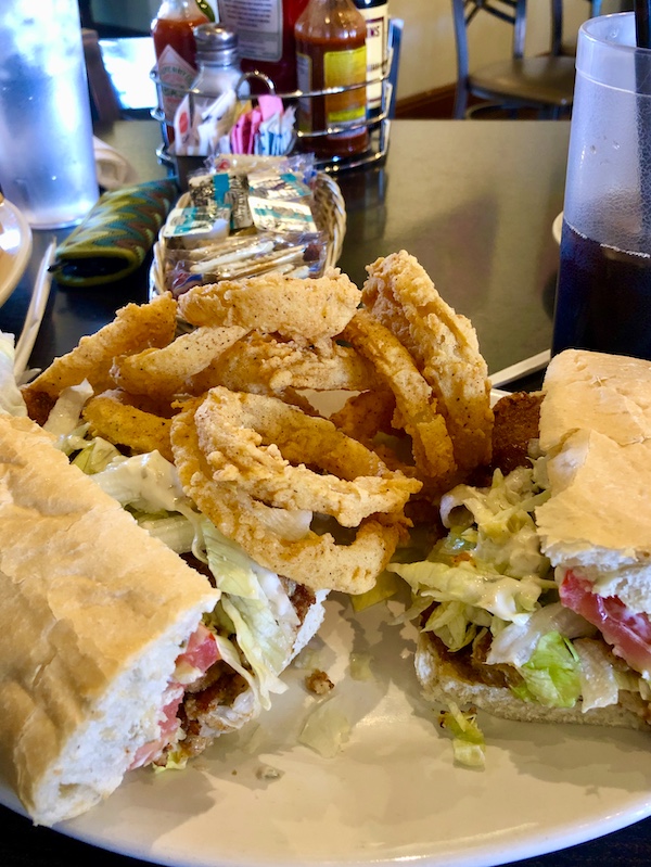 A plate topped with a sandwich cut in half and onion rings in Southwestern Louisiana