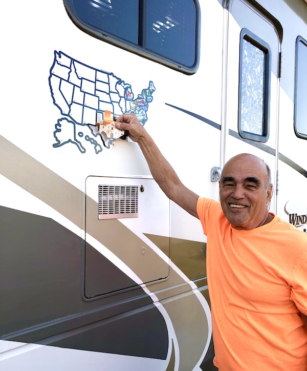 A man in an orange tee shirt placing a Texas at Last! sticker on a map on the side of an RV