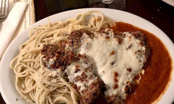 Tidbits of Life in New Orleans a large beige plate topped with veal, tomato sauce, melted cheese and pasta.