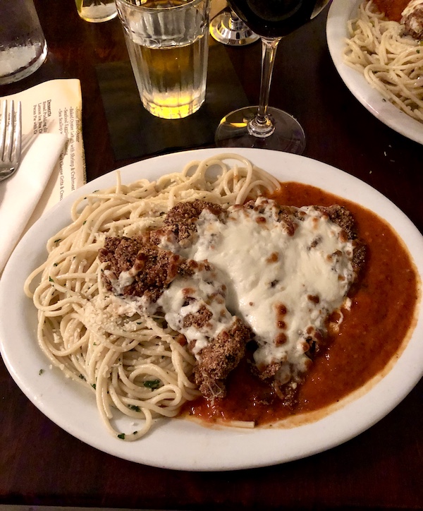 Tidbits of Life in New Orleans a large beige plate topped with veal, tomato sauce, melted cheese and pasta.