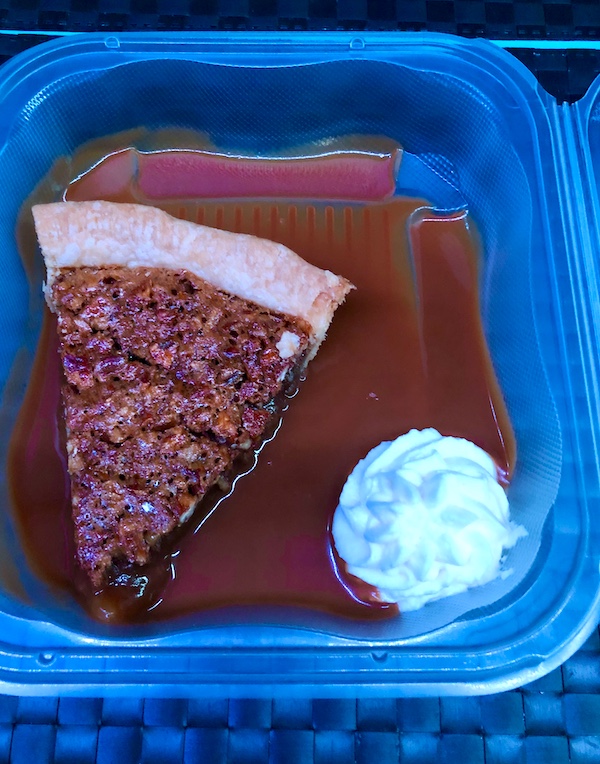 Tidbits of Life in New Orleans A takeout container holding a slice of pecan pie with caramel sauce on the bottom and a swirl of whipped cream in the corner