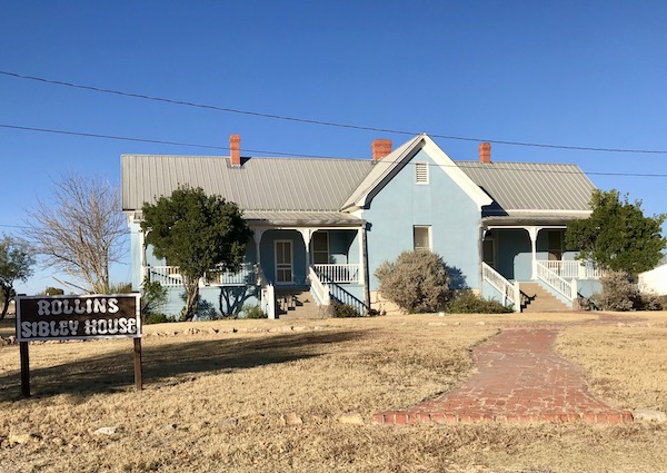 A light blue house with white trim and trees in front at Fort Stockton Texas