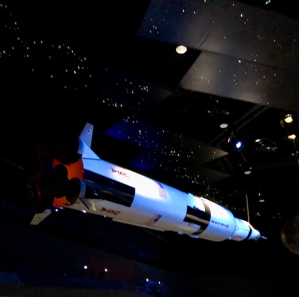 A space craft hanging from a star studding sky (ceiling) at NASA Space Center Houston