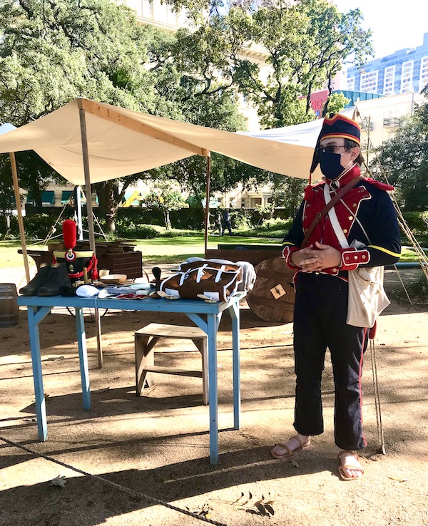 A man in uniform standing by a table with equipment helps us Remember the Alamo
