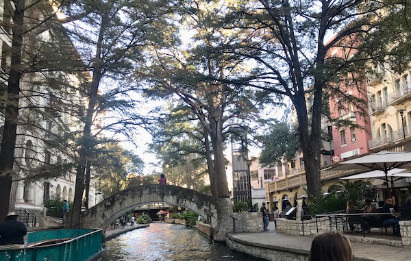 An arched bridge across the river with trees along our San Antonio River Cruise