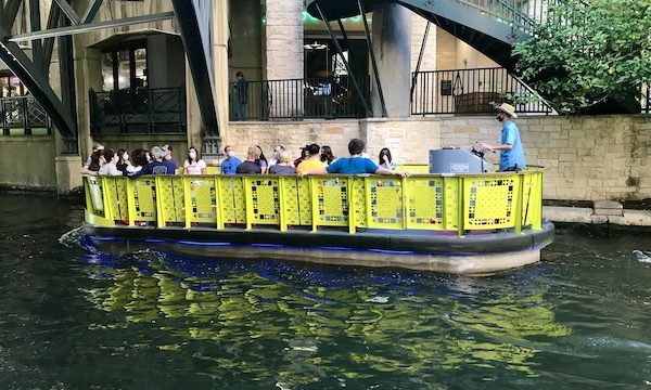 A bright yellow river boat with passengers along our San Antonio River Cruise