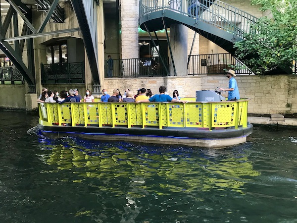 A bright yellow river boat with passengers along our San Antonio River Cruise
