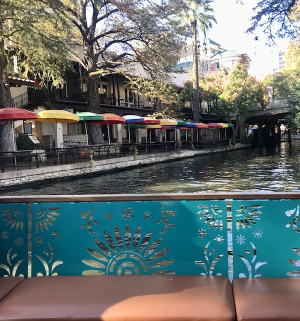 A row of colored umbrella tables in front of a building along the San Antonio River Cruise