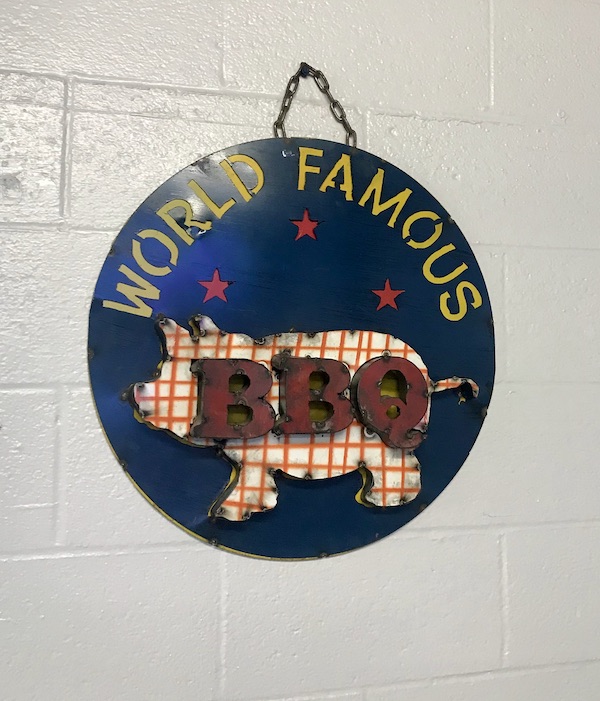 A round sign hanging from a rope loop with a pig and the words World Famous BBQ in Sonora Texas
