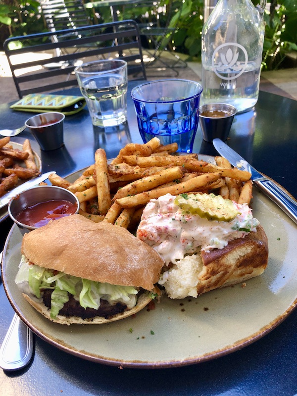 A white plate topped with a half of a cheeseburger and half of a lobster roll with golden French Fries at Southerly Brewery in The Pearl in San Antonio