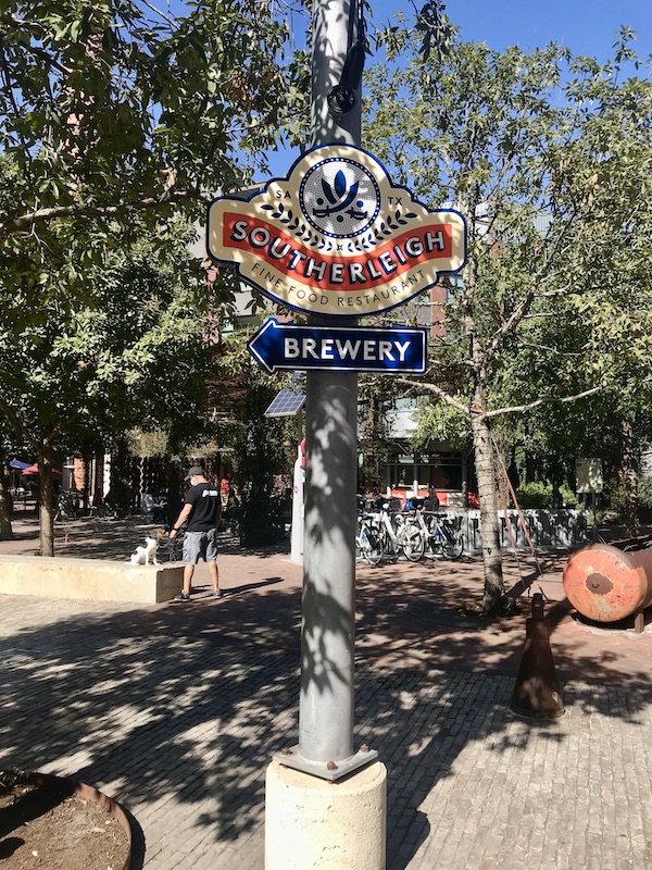 A red and blue sign for Southerleigh Brewery peeks out of the trees in The Pearl in San Antonio