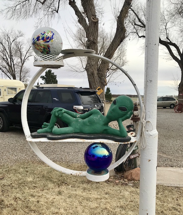 A white post with a ring hanging on the side and a little green man lying on it proving that Aliens Abound in Roswell New Mexico