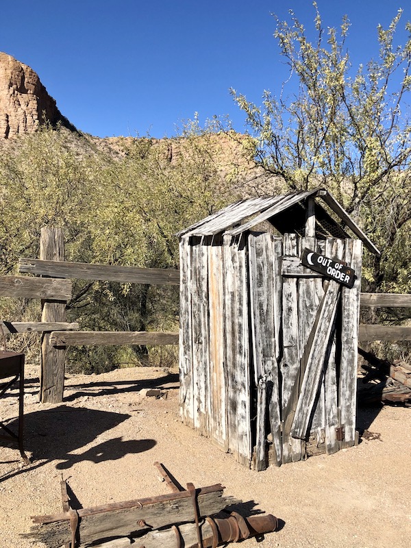 A small wood structure that reads Out of Order in front of trees along the Apache Trail Arizona