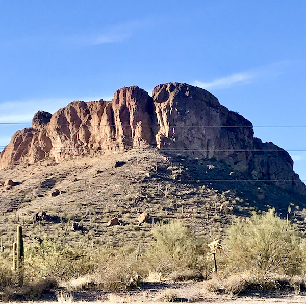 A ruffled rock crowns a mountain top in front of blue sky along the Apache Trail Arizona
