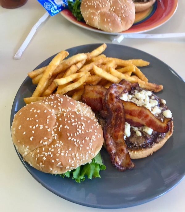 A burger with blue cheese crumbles and bacon with a side of fries ion a blue plate in Bisbee Tombstone and Boot Hill in Arizona