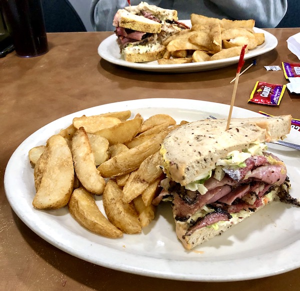 Two white plates topped with sandwiches and French fries on a wood table at Chompie's Deli