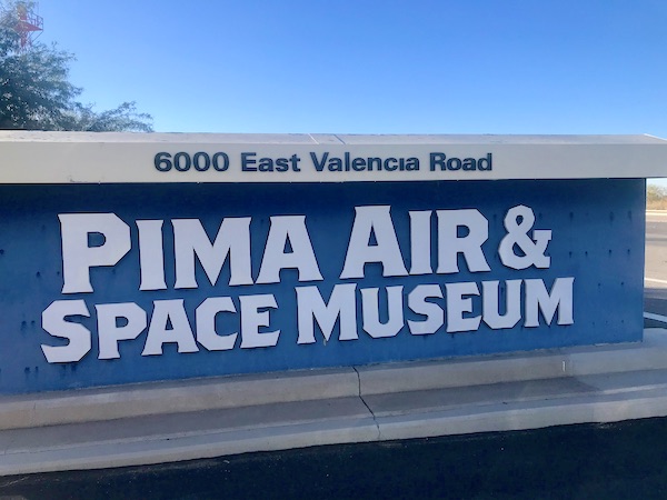 A white stucco wall with white lettering on a blue background welcoming you to the Pima Air and Space Museum