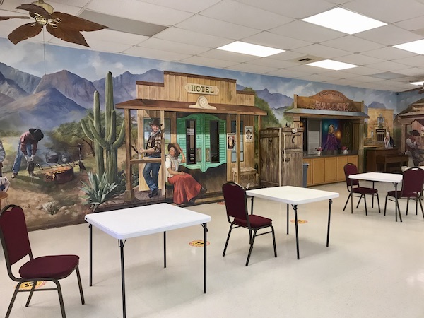 A large room with bridge tables and chairs in front of an old west mural at Rincon Country East RV Resort Tucson AZ