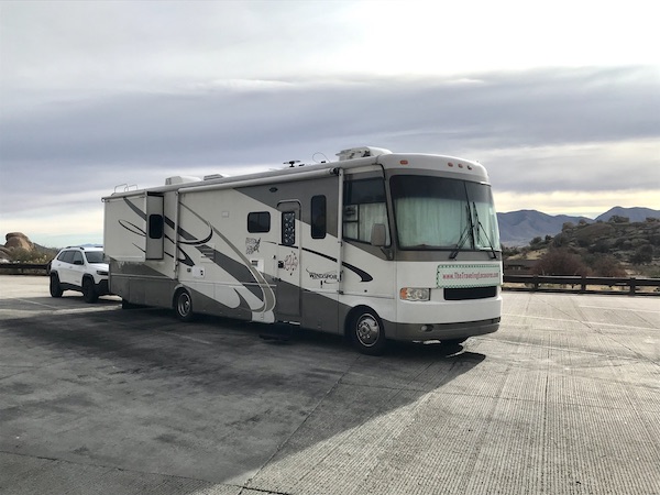 A white and tan RV with a white car in tow parked at a rest stop on the way to Rincon Country East RV Resort Tucson AZ