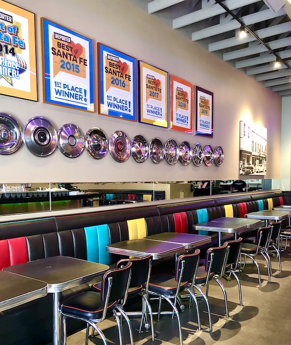 The interior of a restaurant with a colorful banquette and awards and hubcaps hung on the wall at the Plaza Café Santa Fe to Albuquerque New Mexico