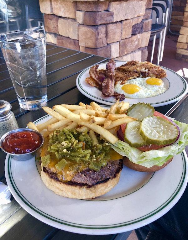 The plate in the foreground is topped with a cheeseburger, green chiles, lettuce, pickles and fries at the Plaza Café. Behind it is a plate of eggs, bacon and potatoes.