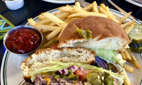 A plate with a burger cut in half, fries and ketchup in the foreground. A plate of fluffy pancakes in the background where we ate when we drove from Santa Fe to Albuquerque New Mexico