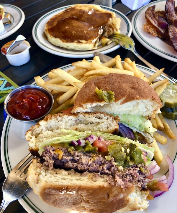 A plate with a burger cut in half, fries and ketchup in the foreground. A plate of fluffy pancakes in the background where we ate when we drove from Santa Fe to Albuquerque New Mexico