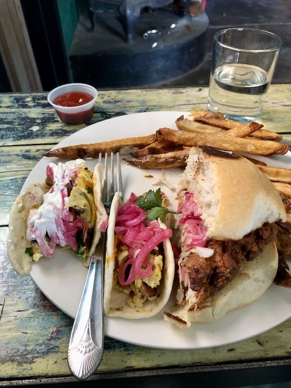 A white plate topped with 2 breakfast tacos and half of a fried chicken sandwich and fries at The Waterstop Marfa Texas