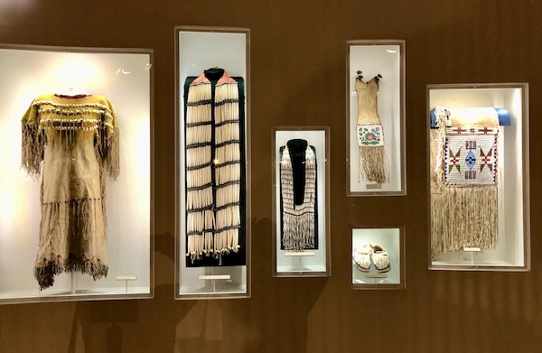 A dark wood wall with alcoves displaying native American clothing and beaded jewelry at the Arizona Museum of Natural History