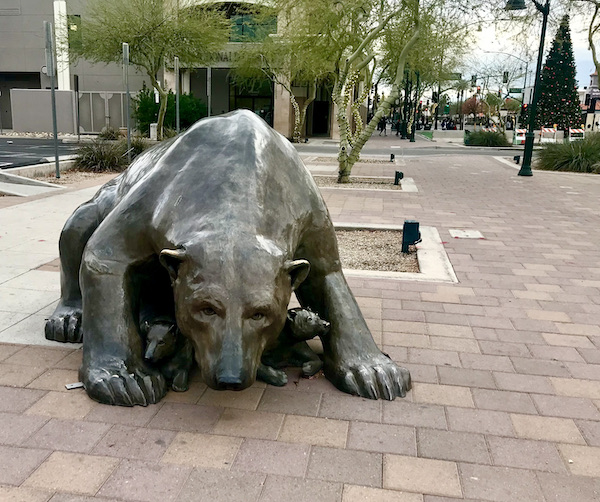 A landscaped pavered park with a sculpture of a mama bear protecting her cubs just outside the Arizona Museum of Natural History