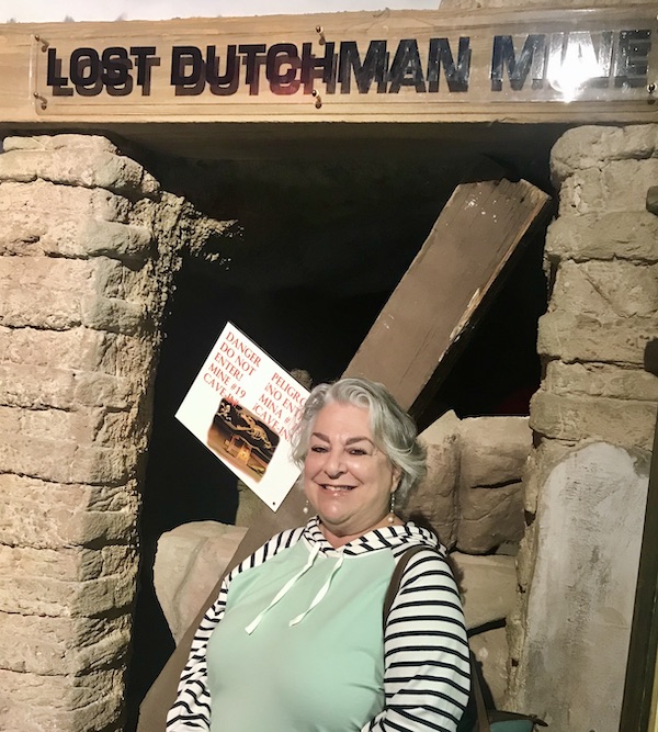 A woman with silver hair in front of the entry to the Lost Dutchman Mine at the The Fremont Street Experience located in downtown Las Vegas Nevada. Visit https://TheTravelingLocavores.combo follow our adventures #downtownlasvegas #fremontstreetexperiance #RVTravels #LasVegas #TheTravelingLocavores #Wanderlust #heartattackgrill #whitecastleburgers #goldennugget #Foodblog #Travel #neonlights