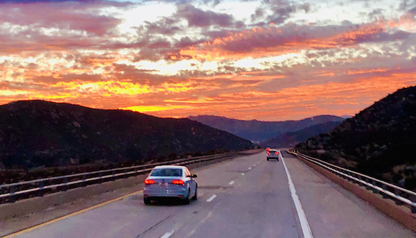 California Here We Come, cars on a highway with the setting sun creating a multicolored sky.
