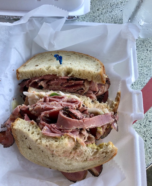 A white styrofoam clamshell with a pastrami sandwich eaten en route Coast to Coast We Did It!