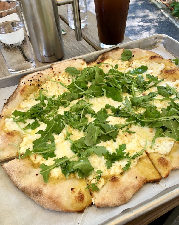 An oval white pizza topped with greens en route Coast to Coast We Did It!
