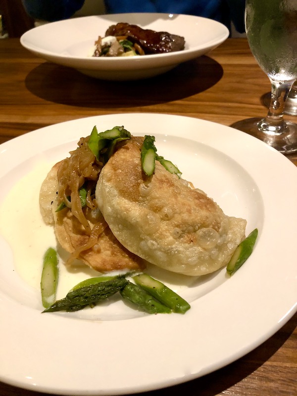 A shallow white bowl filled with dumplings and green leaves eaten en route Coast to Coast We Did It!