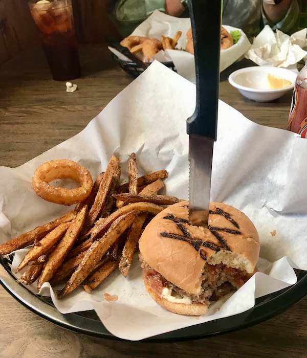 A napkin topped basket filled with a burger with a knife in it and fries eaten en route Coast to Coast We Did It!