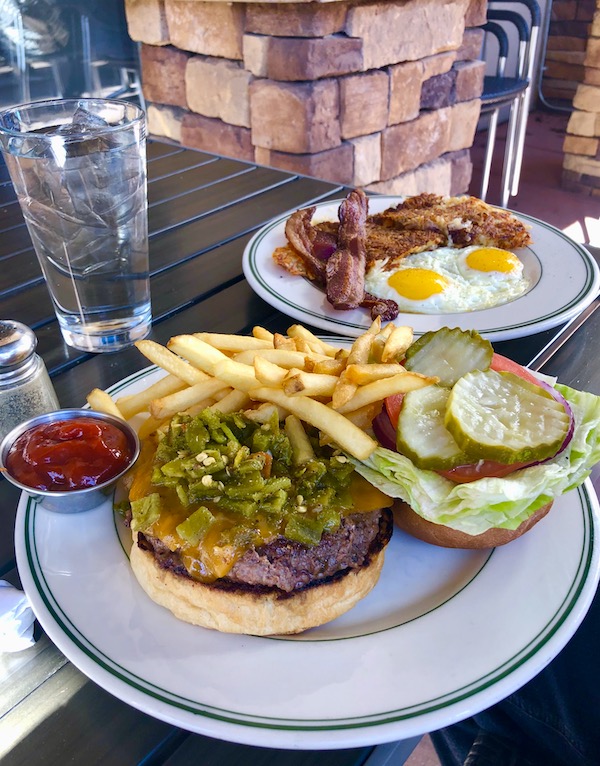 A white plate topped with a burger in a bun with green chilis, lettuce, tomato, pickle slices and fries eaten en route Coast to Coast We Did It!