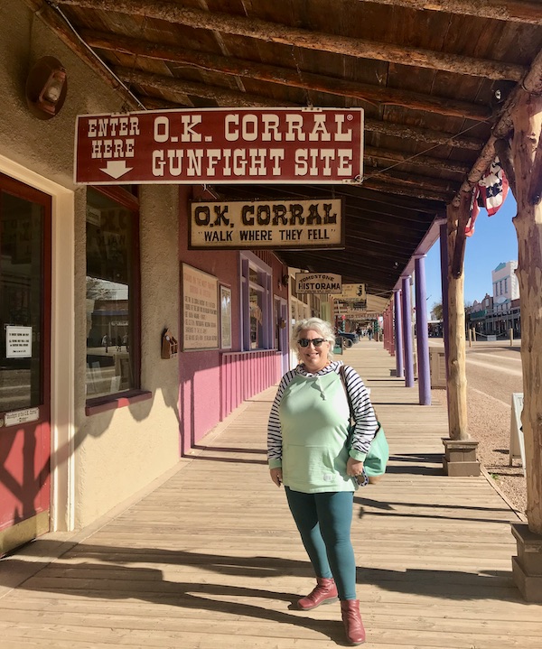 A woman in a mint top standing on an old west walkway by the Gunfight at OK Corral sign en route Coast to Coast We Did It!