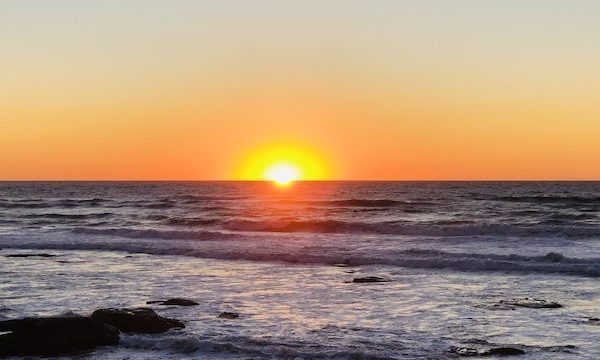 Bright orange sun setting on inky ocean horizon after going