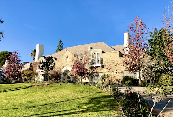 A tan stone mansion set back on a beautiful green lawn in Opulent Beverly Hills California