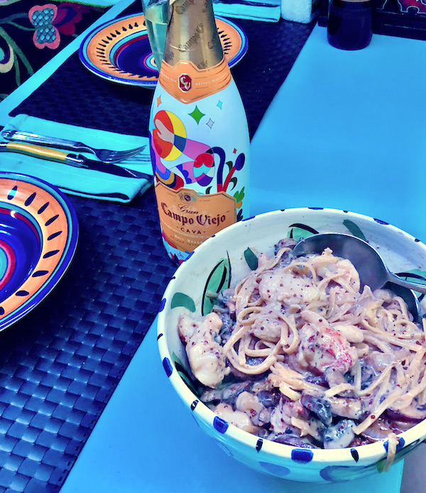 A bowl of pasta with lobster chunks and a bottle of Cava on a dining table in San Diego California