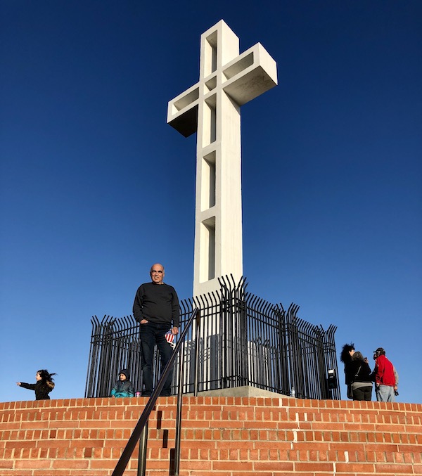 A man standing on steps leading up to a huge white cross in San Diego California
