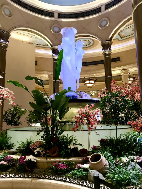 A tall white sculpture lit in lavender land surrounded by plants at the Venetian home to Thomas Keller's Bouchon Las Vegas