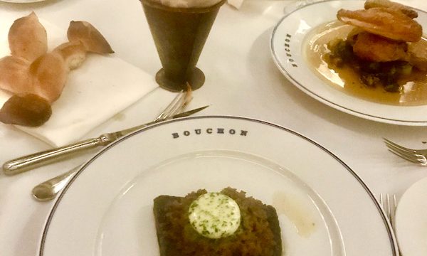 A white tablecloth topped with several plates of food and a cone of fries at Thomas Keller's Bouchon Las Vegas
