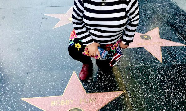 A woman in a striped blouse kneeling by a pink star on a walk of fame during A Day in LaLa Land