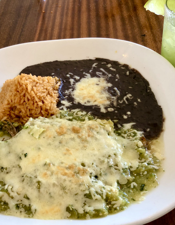 A large white plate topped with lots of cheesy green enchiladas, a pyramid of red rice and a pool of black beans topped with cheese enjoy during A Day with Friends in Windsor California